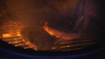 Ein Fleisch auf einem Gasgrill mit offenen Flammen wird mit einem Metallspatel gekocht.