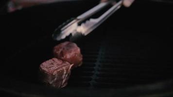 uma carne em uma churrasqueira a gás com chamas abertas é cozida com uma espátula de metal.