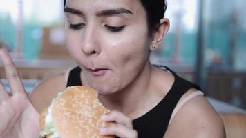 muito jovem latina mulher engraçada comendo hambúrguer ao ar livre na rua. comida rápida video
