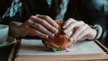 O hambúrguer saboroso fica ótimo em uma bandeja de madeira. uma mulher pega as mãos dele e vai comer