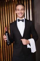 Handsome waiter holding bottle of red wine and towel photo