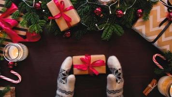 Draufsicht auf Hände in Fäustlingen Weihnachtsgeschenk mit einem roten Band auf dem Tisch gebunden