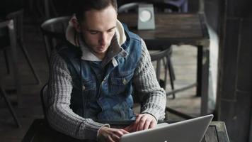 . beau mâle dans la vingtaine utilisant un ordinateur portable à l'intérieur d'un café vide. blogueur tapant un texte. video