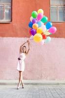 Mujer joven sosteniendo un montón de globos de colores en la calle