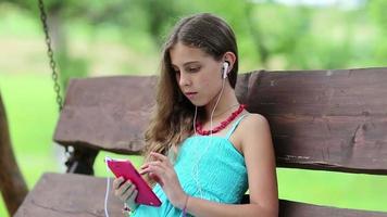 Beautiful girl sits on the swing bench and uses red smartphone video