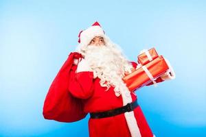 Papá Noel con regalos en las manos sobre fondo azul.