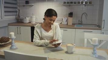 bela jovem afro-americana usando um computador tablet em uma cozinha. video