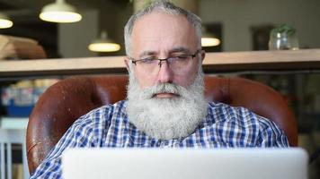 Adult senior bearded man sitting with a laptop video