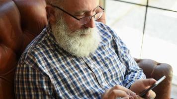 elderly professor is typing a message on a smartphone video