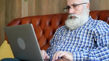 Erwachsener älterer bärtiger Mann, der mit einem Laptop sitzt video