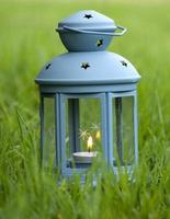 Linterna azul, con vela encendida en el interior, sobre la hierba verde foto