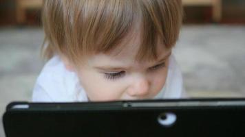 child looks at tablet pc closeup on floor