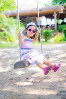 Little girl wear sunglasses on a swing in the park photo