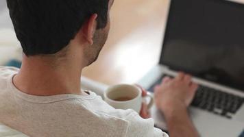 hombre tomando café mientras usa la computadora portátil video