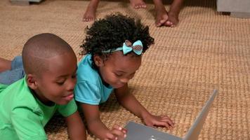 Siblings using laptop on the floor while parents watch video