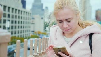 retrato de una mujer joven en nueva york. debe estar en el abrigo rosa sobre un fondo de edificios de Manhattan, escribiendo en el teléfono inteligente video