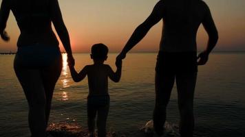 parents jouant au ballon avec son fils en mer au coucher du soleil