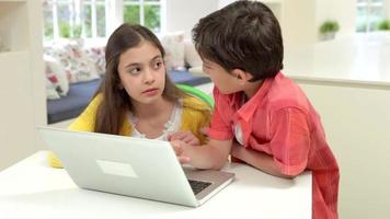 dos niños hispanos usando laptop en casa