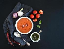 Gazpacho soup in rustic metal bowl with fresh tomatoes, green photo
