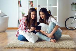 Two beautiful young woman friends using digital tablet at home.