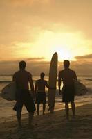 Amigos con tabla de surf viendo el atardecer en la playa foto