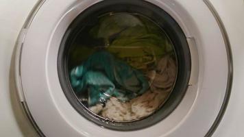 Wet clothes turning in washing machine, view through front glass