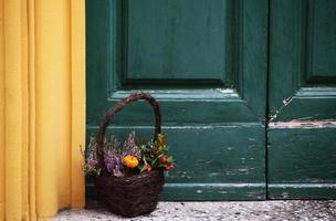 Cesta marrón llena de flores cerca de la colorida puerta foto