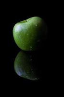 Manzana verde sobre negro de lado con reflexión vertical foto