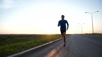 The guy runs along the road at sunset. Front view