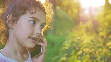 menina adolescente falando ao telefone atrás do pôr do sol hora dourada natureza floresta vídeo em câmera lenta ao ar livre