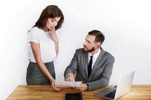 Woman looks shocked while angry businessman points to paper photo