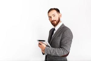 Hombre serio con barba roja posa en traje gris con tableta en la mano foto