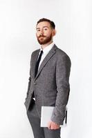 Serious man with red beard poses in gray suit with tablet in his hand