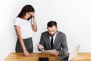 Tired woman stands by businessman while he looks angry at paperwork photo