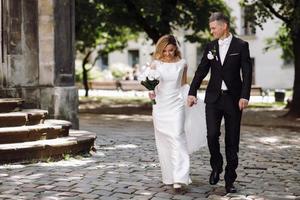 Groom holds bride's hand while walking on cobblestone path photo