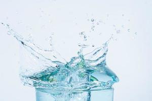 Salpicaduras de agua en un vaso sobre fondo blanco. foto