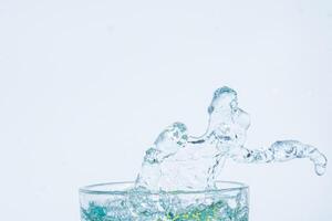 Salpicaduras de agua en un vaso sobre fondo blanco. foto