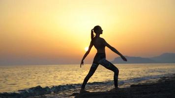 junge Frau der Silhouette, die Yoga am Strand bei Sonnenuntergang praktiziert