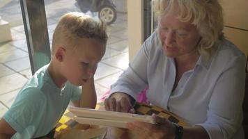 Grandmother and grandson with pad in cafe video