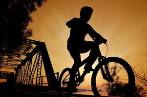 niño montando bicicleta silueta. puesta de sol foto