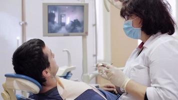El dentista comprueba los dientes del paciente masculino por espejo dental video