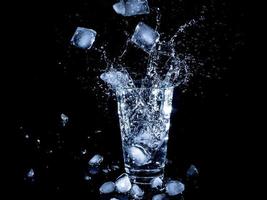 cubitos de hielo cayeron en un vaso transparente con agua foto