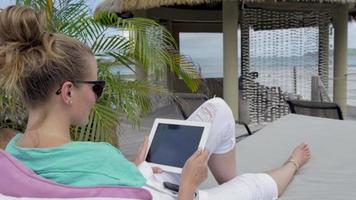 junge Frau, die im Hotelliegeplatz mit digitalem Tablett während des Urlaubs sitzt.