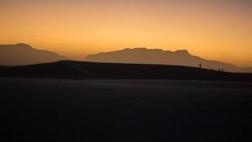 winderige woestijn tijdens zonsondergang met mensensilhouetten