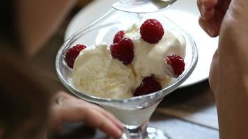 Girl eating vanilla icecream dessert with raspberries in glass bowl in cafe