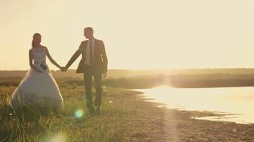 Braut und Bräutigam rennen durch das Feld, um die Sonne bei Sonnenuntergang zu treffen video