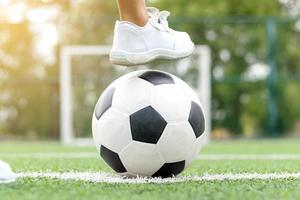 Pies de un niño vestido con zapatillas blancas pisando una pelota de fútbol foto