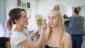transformación. En el moderno salón de belleza, un maquillador profesional prepara la imagen de una atractiva rubia.