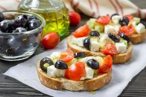 Greek style crostini with feta cheese, tomatoes, cucumber, olives, herbs photo