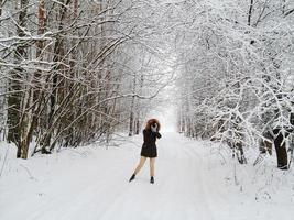 Latvia, 2020 - Woman in a black parka taking a photo in a snowy landscape